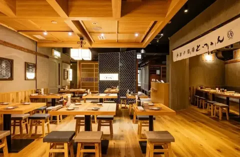 池袋東口の餃子酒場肉汁とっつぁんの木目調の店内にテーブル席と丸椅子が並ぶ様子の写真