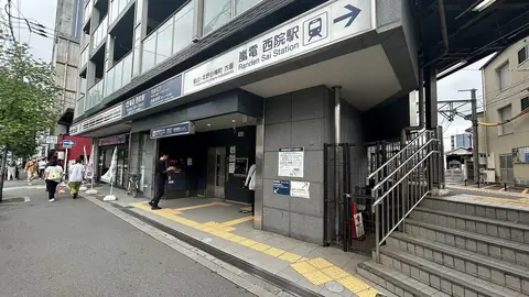 京都市の阪急西院駅北口がある駅ビルの外観と、駅前の道路や通行人が写った街並みの写真