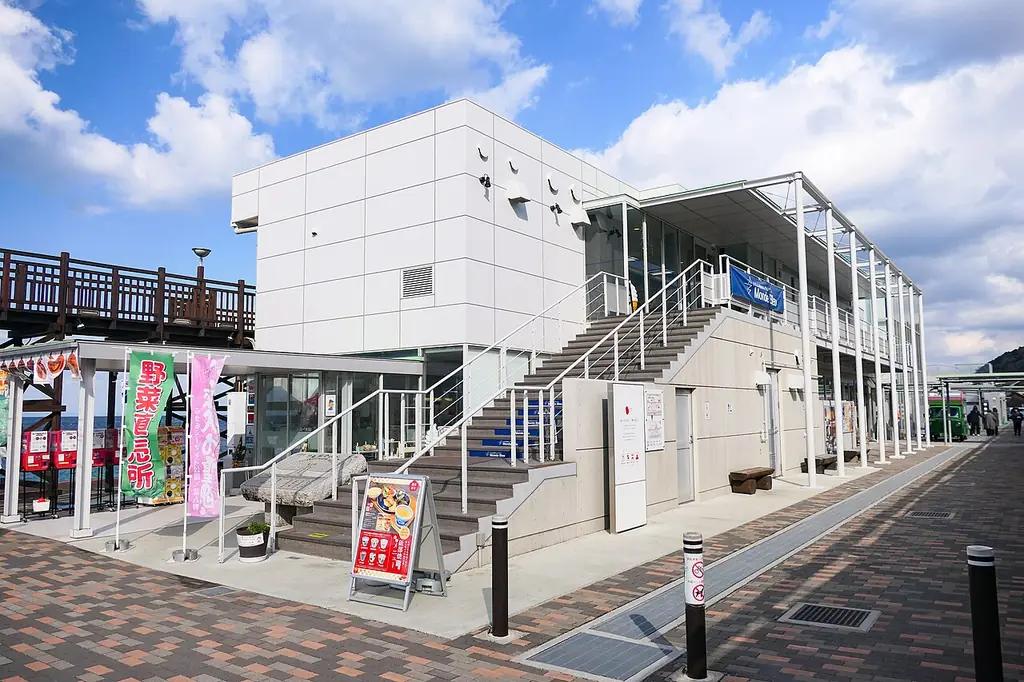 道の駅ふたみ（伊予市）の、外階段のある白い二階建ての建物とのぼり旗と案内板と前の通路の写真
