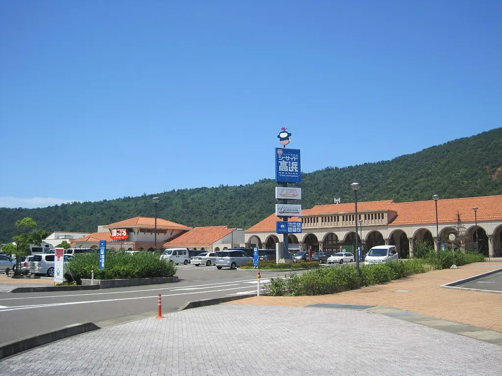 道の駅シーサイド高浜（高浜町）の、道の駅の案内塔の奥に並ぶオレンジの屋根の建物と山の写真