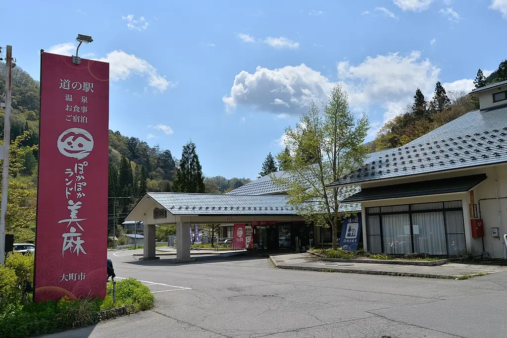 道の駅ぽかぽかランド美麻（大町市）の、「道の駅」と書かれた赤い縦長の看板と屋根付きの入口がある建物の写真