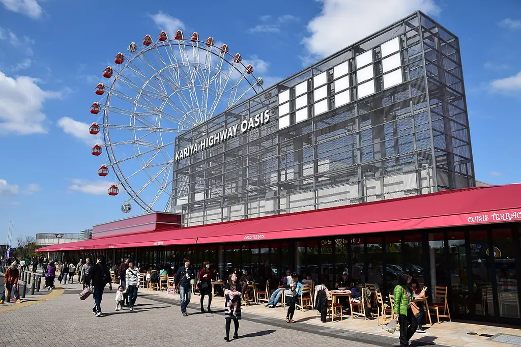 刈谷パーキングエリアの、大きな観覧車と「KARIYA HIGHWAY OASIS」の文字が付いた建物と、前を歩く人たちの写真