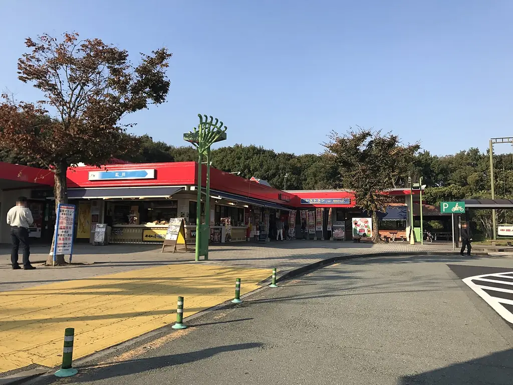 広川サービスエリアの、赤いひさしの店が横に並ぶ建物と、前の広場に立つ木と人の写真