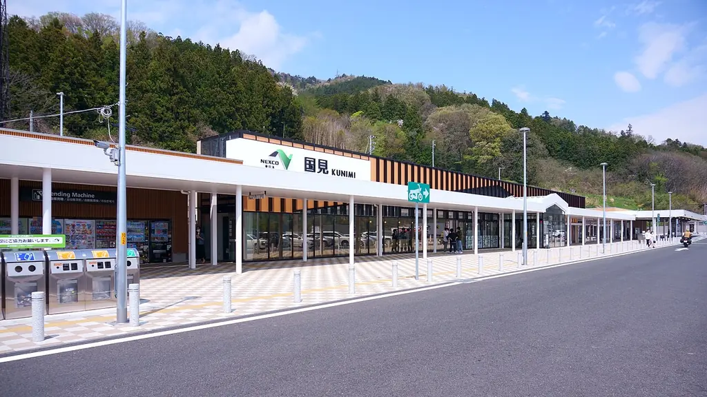国見サービスエリアの、「国見」の看板が付いた横に長い建物と白い屋根の通路、手前の車道の写真