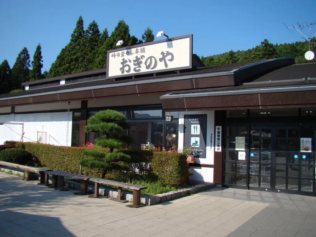 横川サービスエリア（上り）の、「おぎのや」の看板が付いた建物と、前の松の植え込みとベンチの写真