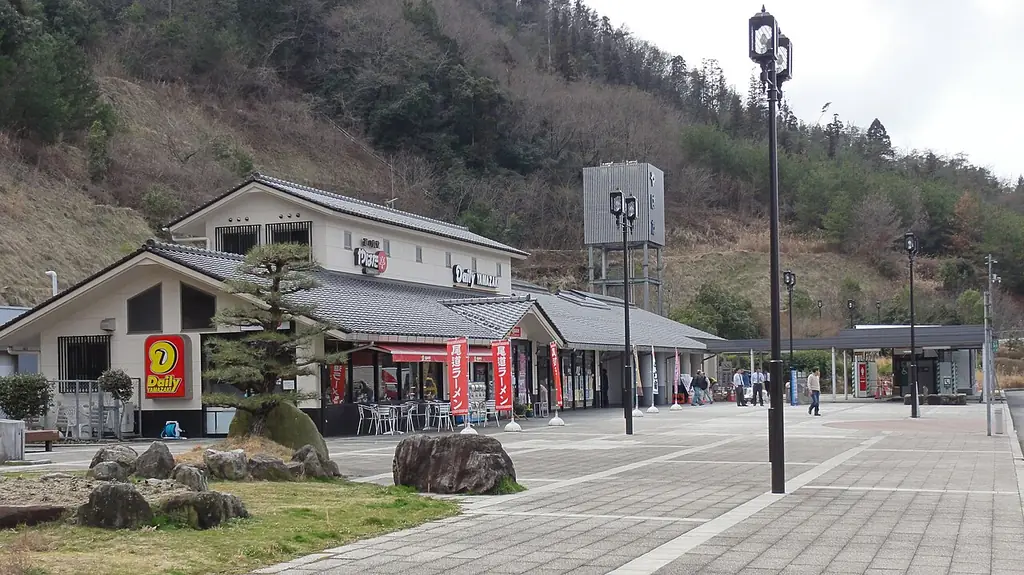 八幡パーキングエリアの、瓦屋根の建物と石の置かれた庭、前の広場と照明柱、うしろの山の写真