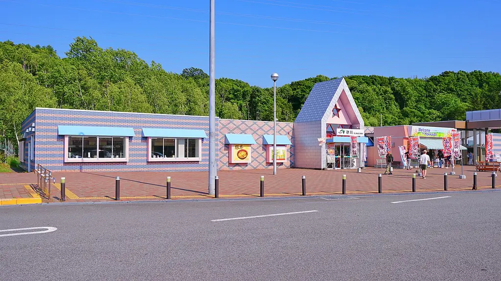 砂川サービスエリア（上り）の、薄い紫色の壁に三角屋根の入口が付いた建物と、前の駐車場の写真