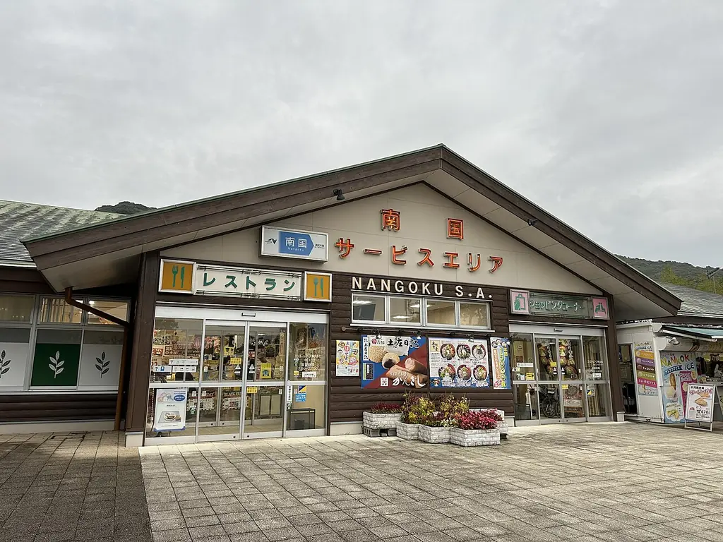 南国サービスエリア（上り）の、「南国サービスエリア」の看板が付いた三角屋根の建物と店先の写真
