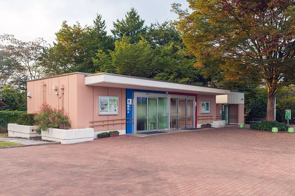 泉パーキングエリアの、ピンクの壁にガラスの入口が付いた平屋の建物と、前のレンガ色の広場と紅葉した木の写真
