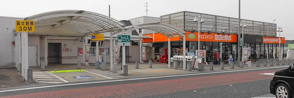 天理パーキングエリアの、丸い屋根の通路とオレンジ色の看板の店が横に並ぶ建物の写真