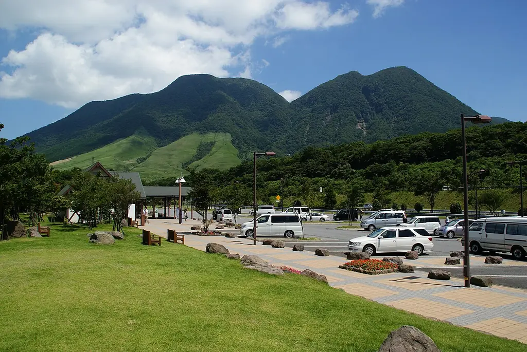 由布岳パーキングエリアの、芝生の広場と駐車場に止まる車、うしろにそびえる大きな山の写真
