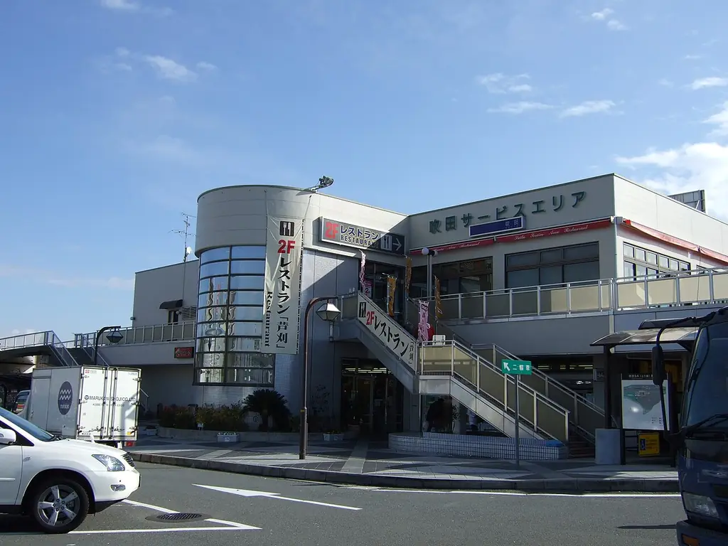 吹田サービスエリアの、「吹田サービスエリア」の看板が付いた建物と外の階段、手前の車の写真