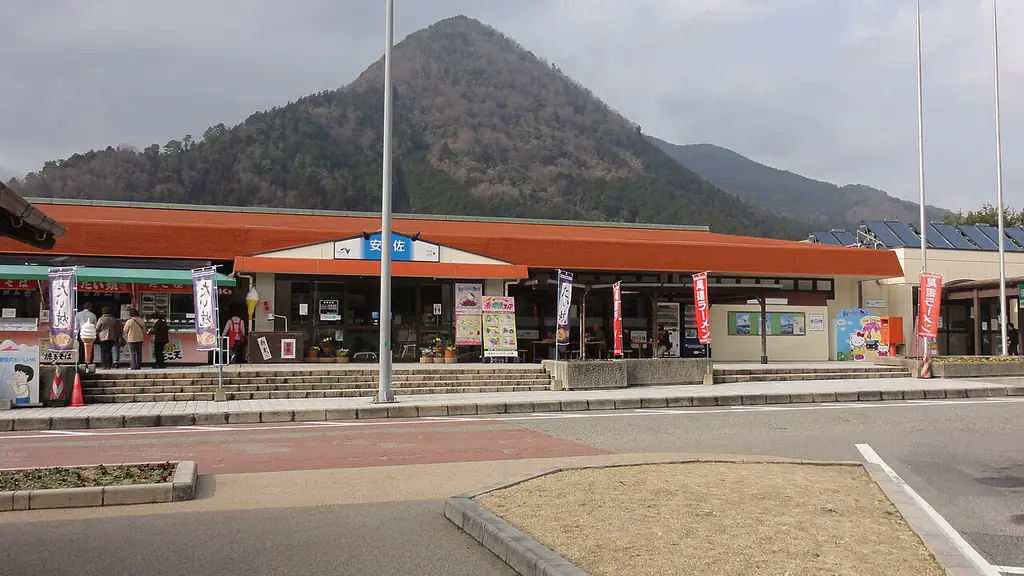 安佐サービスエリア（上り）の、オレンジ色の屋根の店が並ぶ建物と旗ざお、うしろにそびえる山の写真