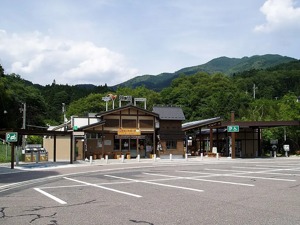神坂パーキングエリア（東京方面）の、木造風の建物と車の少ない駐車場、うしろに広がる緑の山の写真