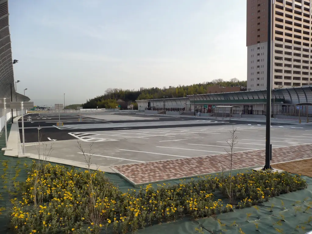 京田辺パーキングエリアの北側の、白線の引かれた広い駐車場と花壇、奥の高い建物の写真