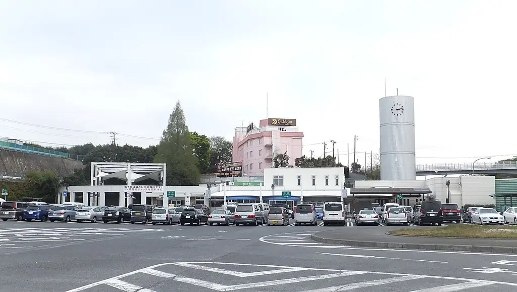 保土ヶ谷パーキングエリアの、車が並ぶ広い駐車場と、奥の白い建物とピンクの建物、白い塔の写真