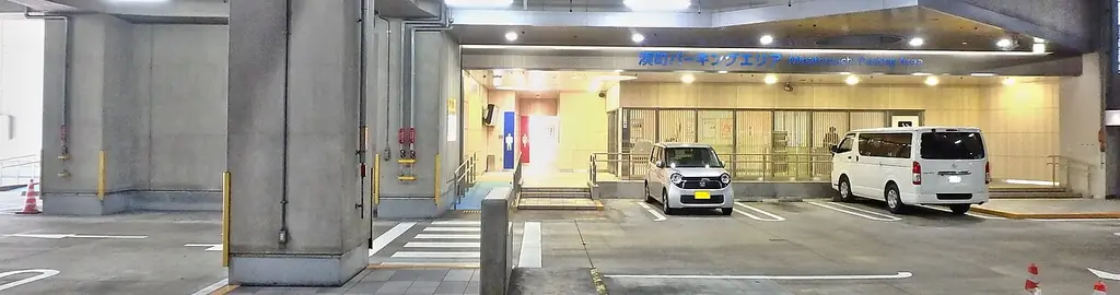 湊町パーキングエリアの、柱が並ぶ屋内の駐車スペースと、奥の明るい休憩所の入口と止まる車の写真