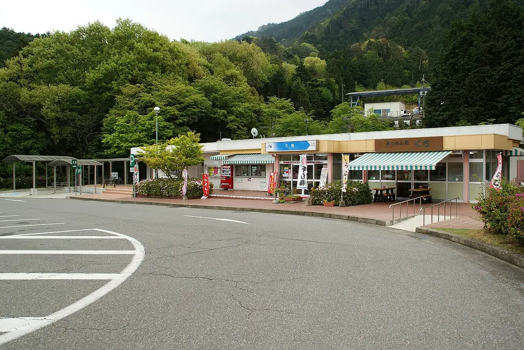 久地パーキングエリアの、店が並ぶ平屋の建物と、前のカーブする車道、うしろの木の茂った山の写真