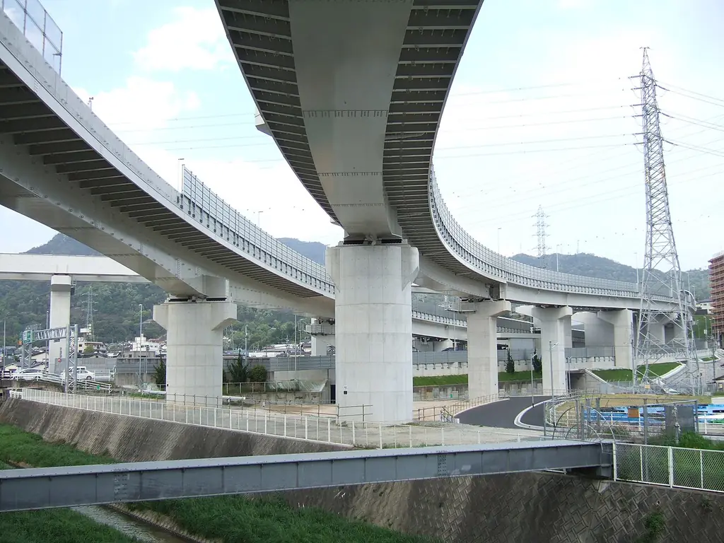 温品ジャンクションの、太いコンクリートの柱に支えられて大きく曲がる高架の道路と、右に立つ送電線の鉄塔の写真