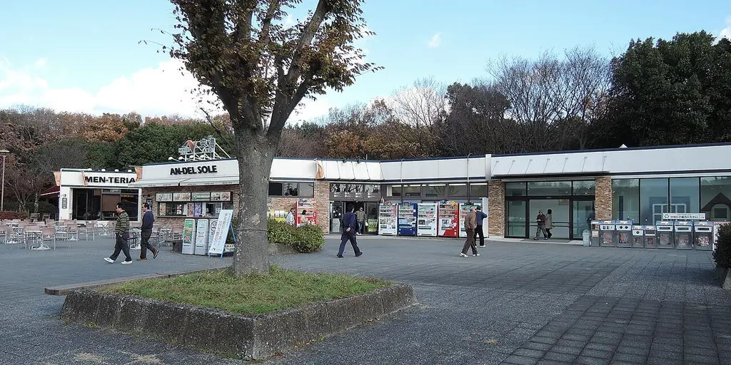 安濃サービスエリア（下り）の、手前の大きな木と石だたみの広場、奥に並ぶ店の建物と歩く人たちの写真
