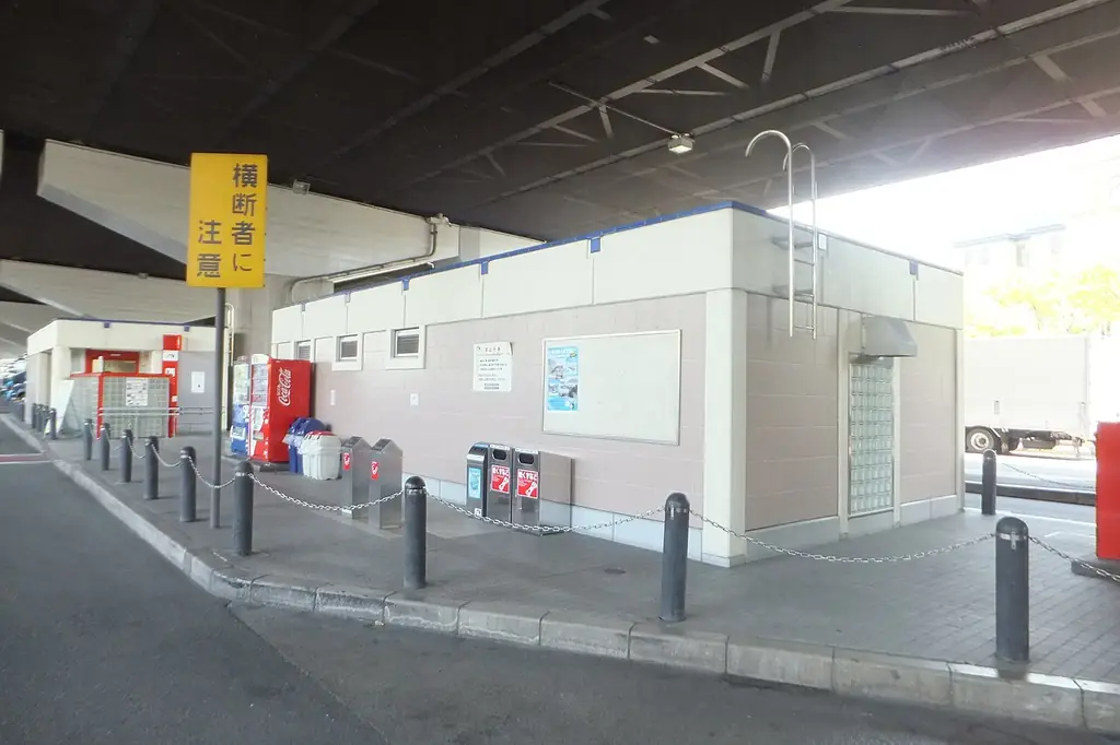 東大阪パーキングエリアの、高架の下にある白い建物と自販機、前の歩道に並ぶ車止めの写真