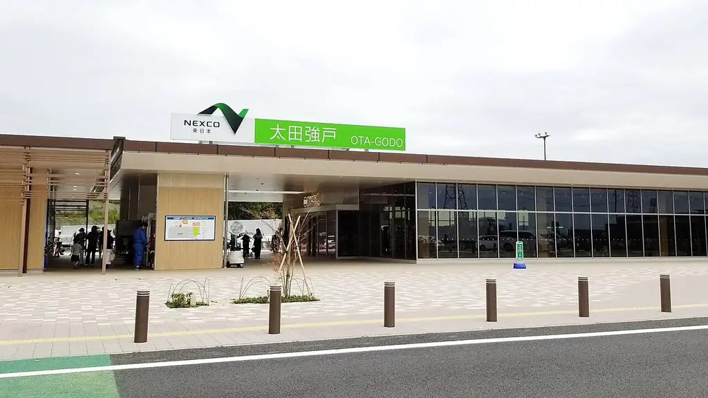 太田強戸パーキングエリアの、「太田強戸」の看板が付いた横に長いガラス張りの建物と、前に並ぶ車止めの写真