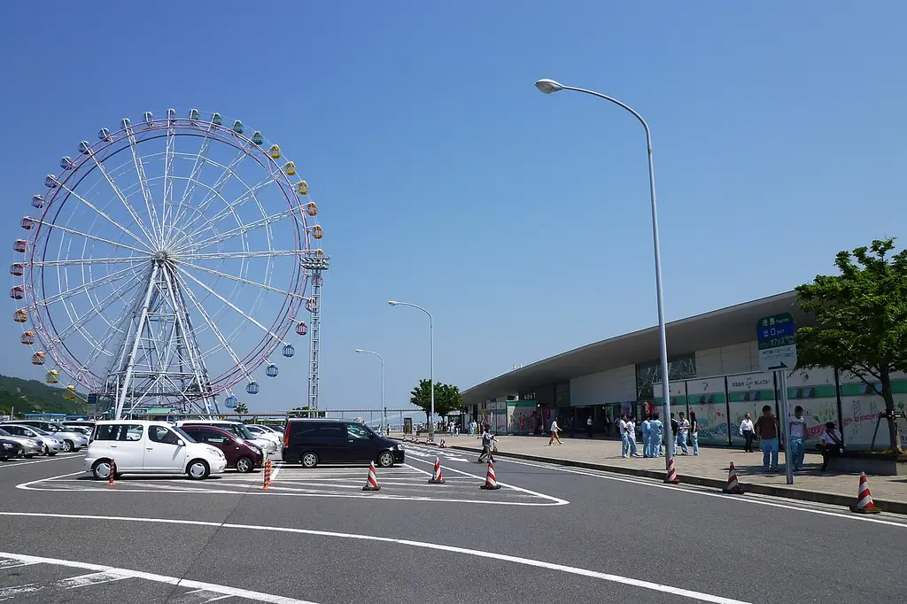 淡路サービスエリアの、大きな観覧車と横に長い建物、手前の駐車場に止まる車と歩く人たちの写真