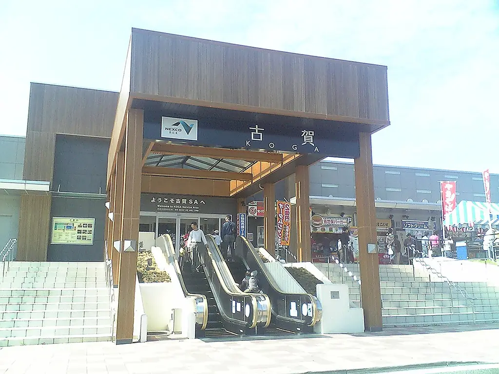 古賀サービスエリアの、「古賀」の看板が付いた木の門のような入口と、上へ向かうエスカレーターと階段の写真