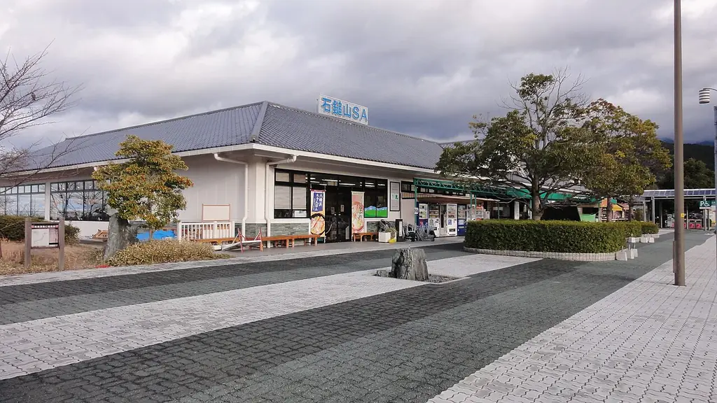 石鎚山サービスエリアの、「石鎚山SA」の看板が付いた建物と、前の木々と広い歩道の写真