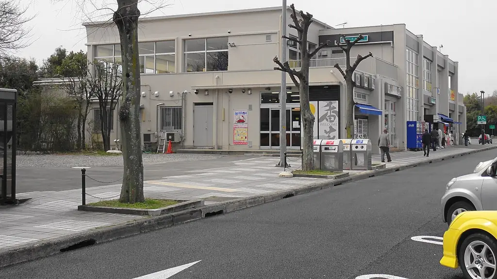 香芝サービスエリアの、2階建ての白い建物と前の歩道、手前に並ぶ木と道路に止まる車の写真