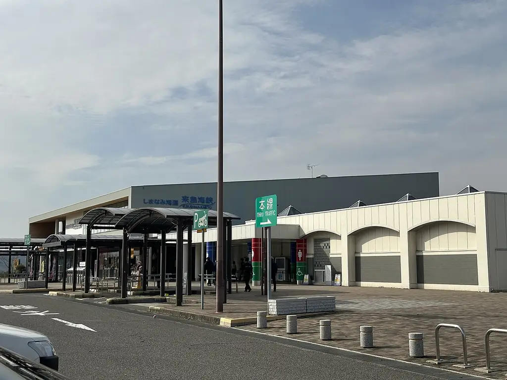 来島海峡サービスエリアの、アーチの窓が並ぶ白い建物と屋根の付いた通路、前の広い駐車場の写真
