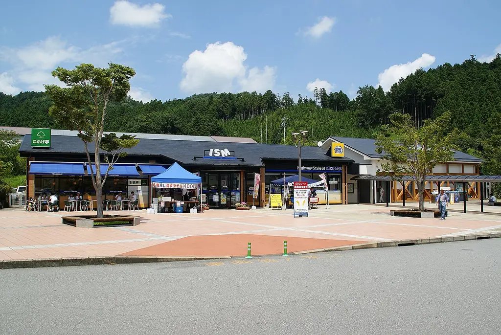 玖珠サービスエリアの、青いひさしの店が並ぶ建物と、前の広場に立つ木とテント、うしろの山の写真