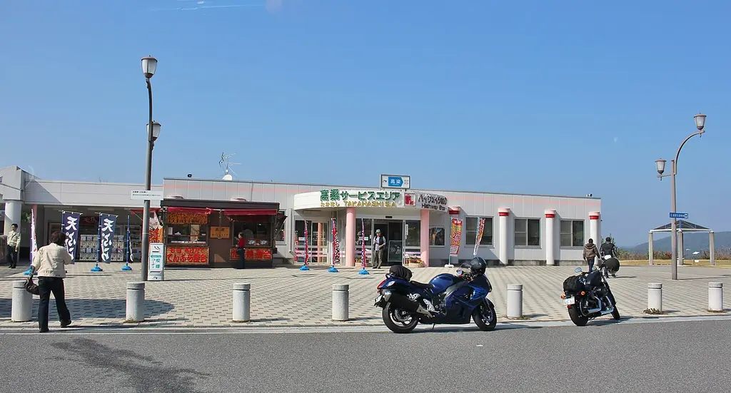高梁サービスエリアの、「高梁サービスエリア」の看板が付いた白い建物と、前に止まるバイクと人の写真
