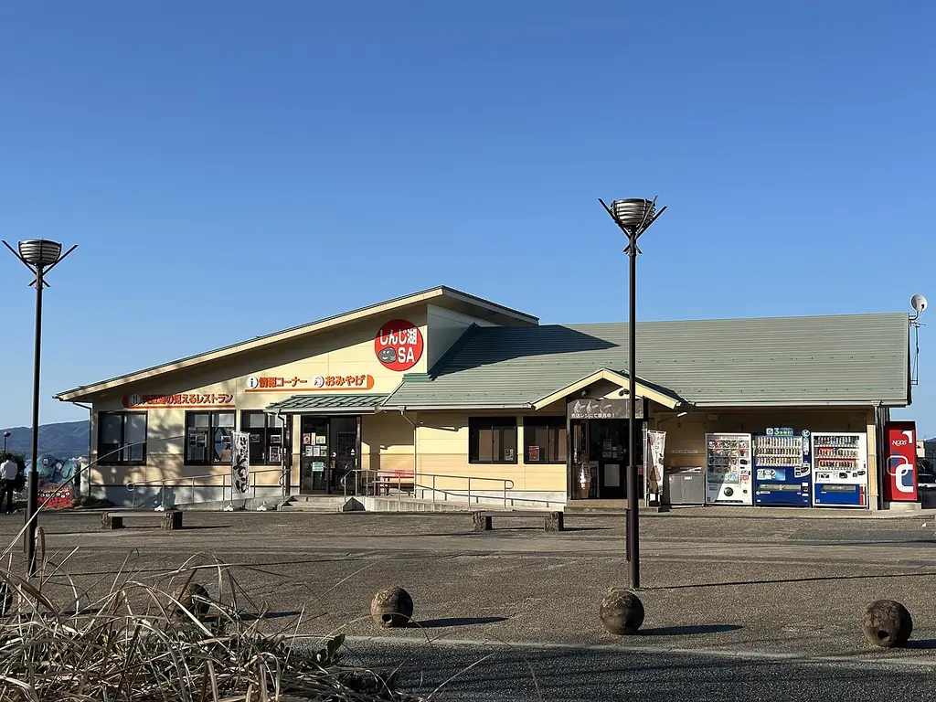 宍道湖サービスエリア（下り）の、緑の屋根の平屋の建物と自販機、前の広場に立つ照明柱の写真