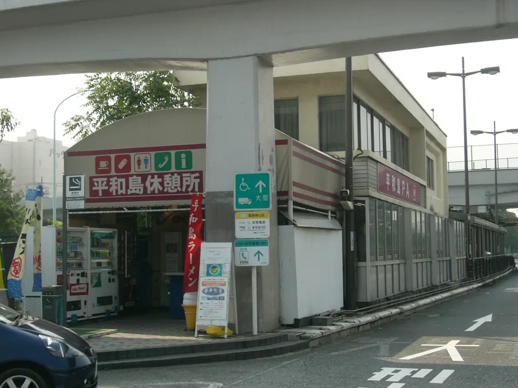 平和島パーキングエリア（下り）の、「平和島休憩所」の看板が付いた建物と自販機、高架の柱の写真