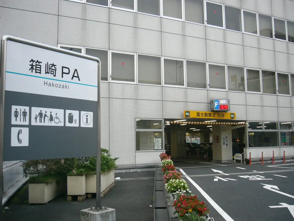 箱崎パーキングエリアの、「箱崎PA」の案内板と白い建物の入口、手前の花の植え込みの写真