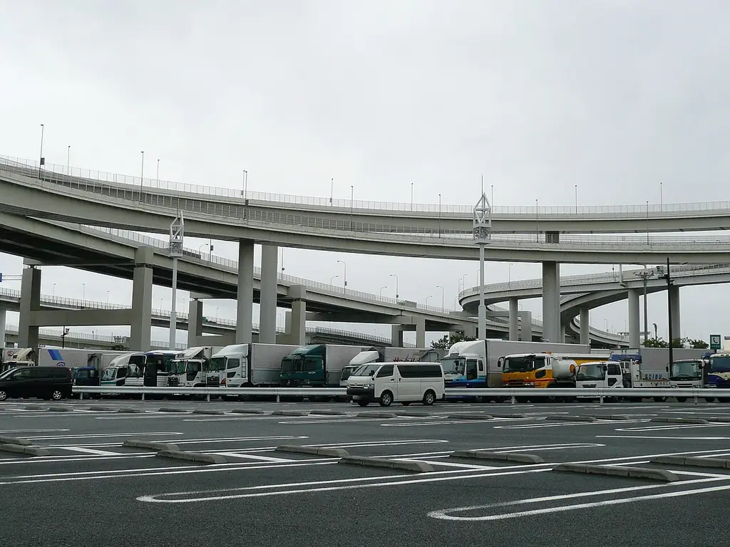 大黒パーキングエリアの、白線の引かれた広い駐車場と止まるトラック、うしろで輪を描く高架の道路の写真