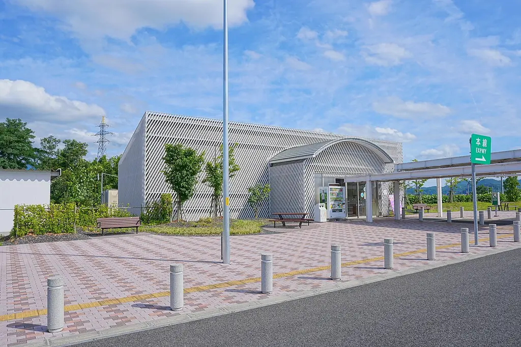山形パーキングエリアの、網目の外壁の建物と屋根の付いた通路、前の広場に並ぶ車止めの写真
