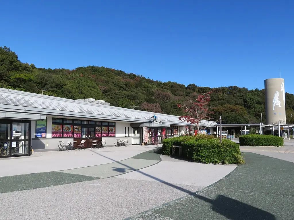上板サービスエリア（上り）の、横に長い建物と植え込みのある広場、うしろの山と白い塔の写真
