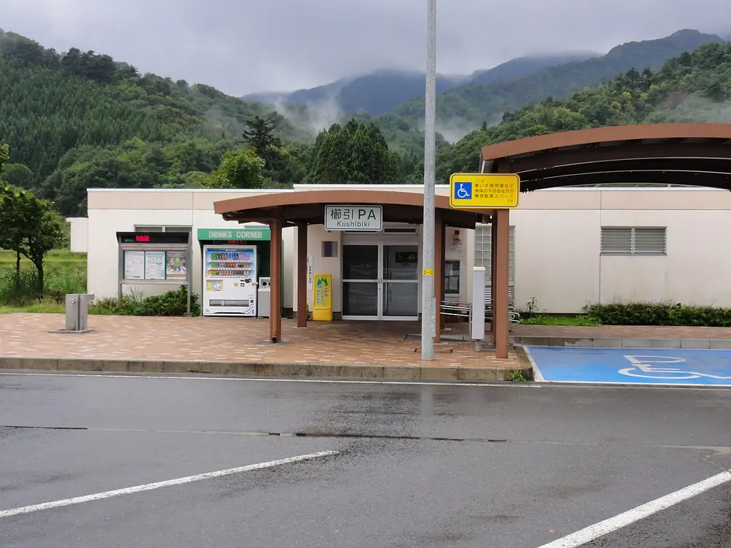 櫛引パーキングエリアの、「櫛引PA」の看板と屋根の付いた小さな建物、自販機と、うしろの山の写真