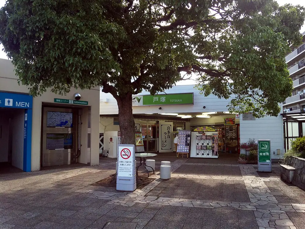 戸塚パーキングエリアの、「戸塚」の看板が付いた建物の入口と、前に立つ大きな木と石だたみの写真