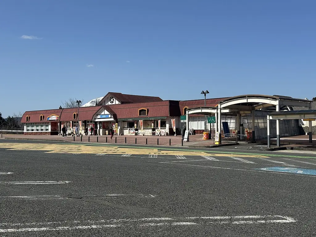 蒜山高原サービスエリア（上り）の、赤い屋根の洋風の建物と屋根の付いた通路、手前の広い駐車場の写真