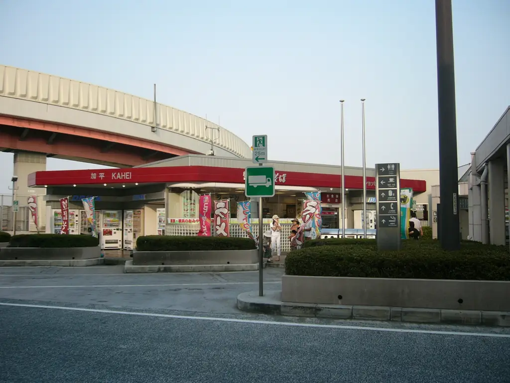 加平パーキングエリアの、赤いひさしの付いた建物と植え込み、うしろを通る高架の道路の写真
