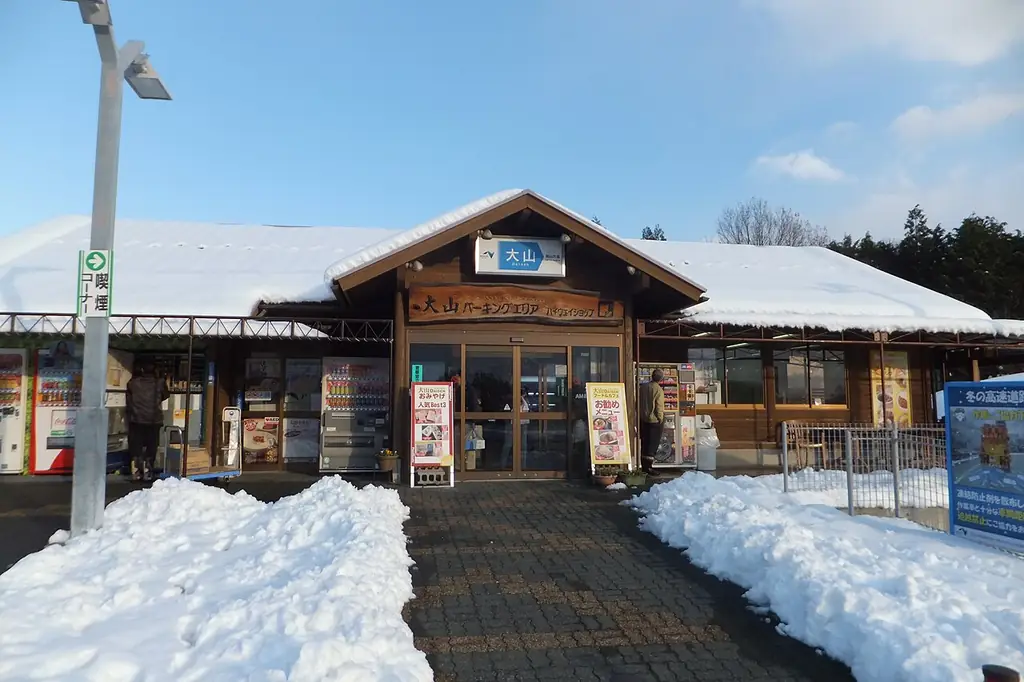 大山パーキングエリアの、雪の積もった屋根の木の建物と入口、手前に積まれた雪の写真