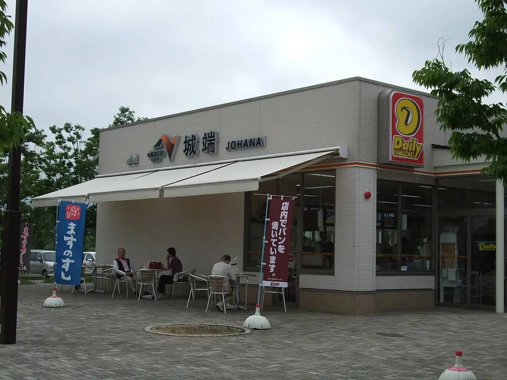 城端サービスエリアの、「城端」の看板が付いた建物と白いひさし、前のテーブル席に座る人たちの写真