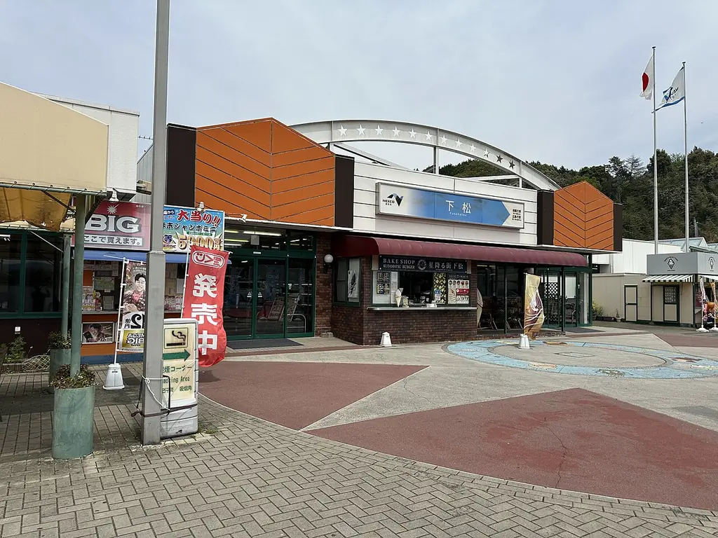 下松サービスエリア（上り）の、「下松」の看板が付いた建物と、のぼりと旗、前の模様のある広場の写真