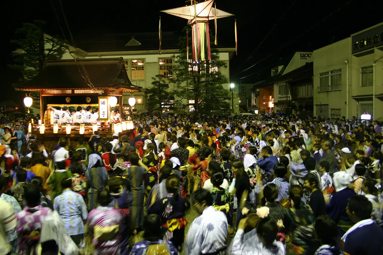 郡上おどりで、切り子灯籠の下、囃子の屋形のまわりで浴衣の人たちが輪になって踊る夜の様子の写真