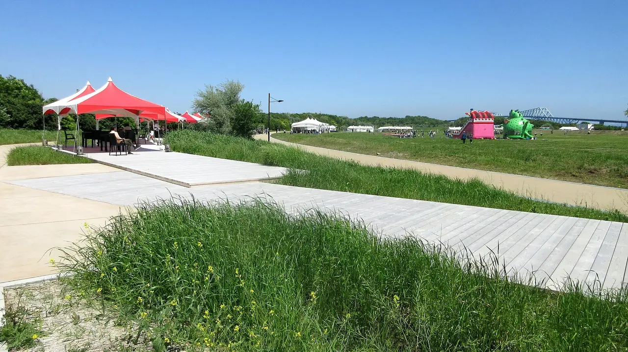 海の森公園（会場）の、ウッドデッキのテラスから見た芝生の広場で、奥に赤や白のテント、遠くに橋が見える様子の写真