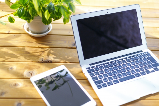 木の机に置いたノートパソコンとタブレットと観葉植物