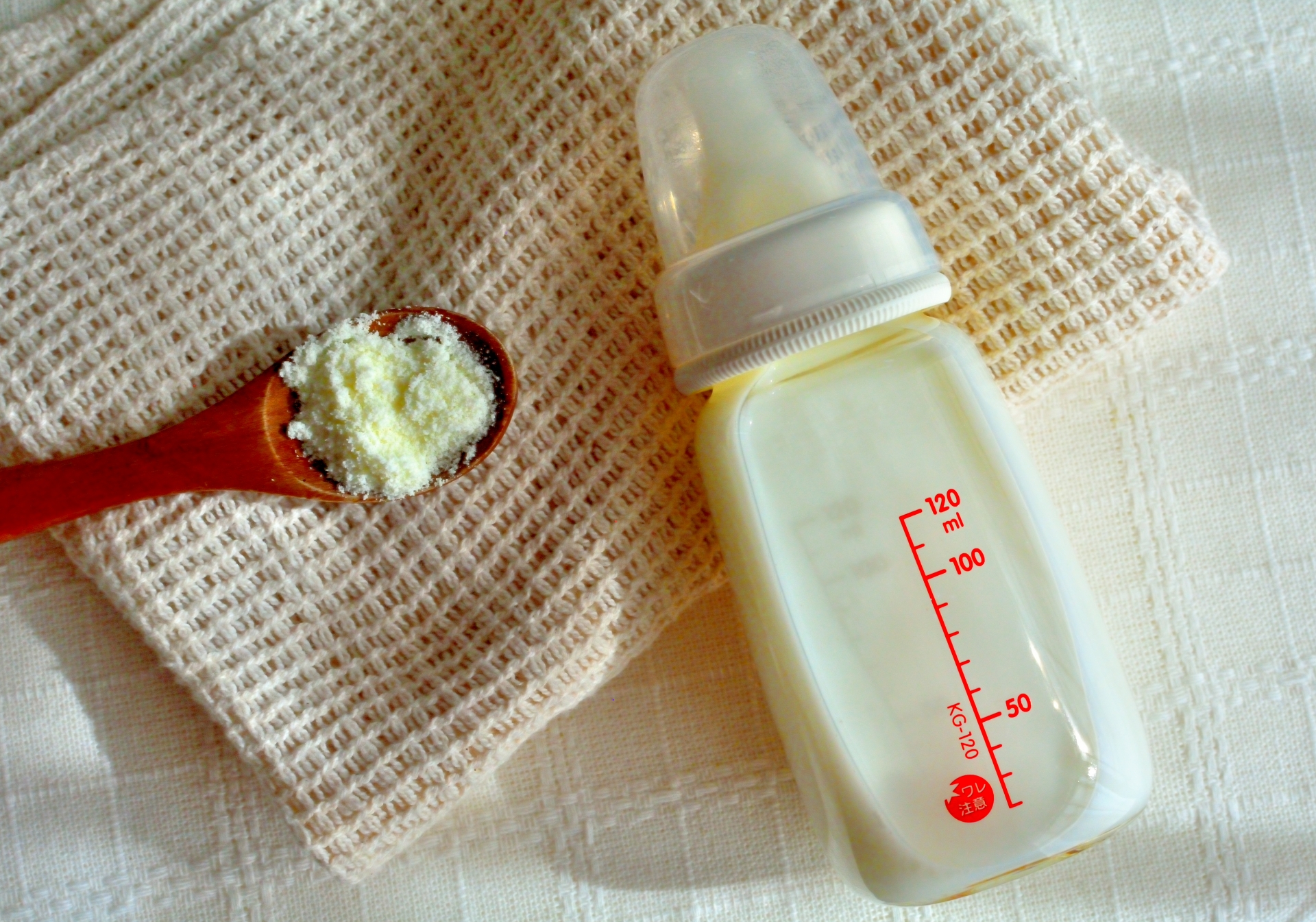 白い布の上に置いた哺乳瓶と、粉ミルクをすくったスプーン